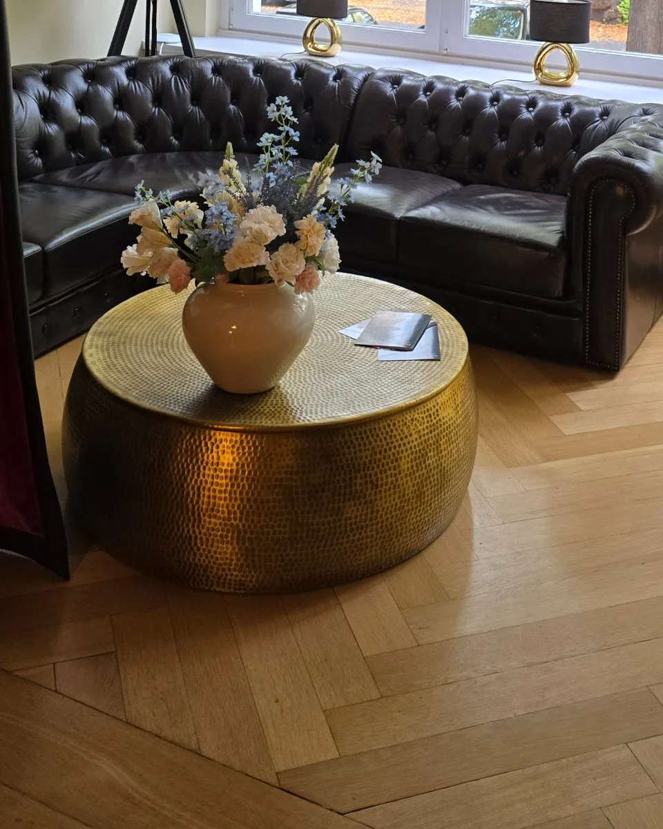 Chesterfield-Sofa und ein Messingtisch mit Blumen am hohen Fenster
